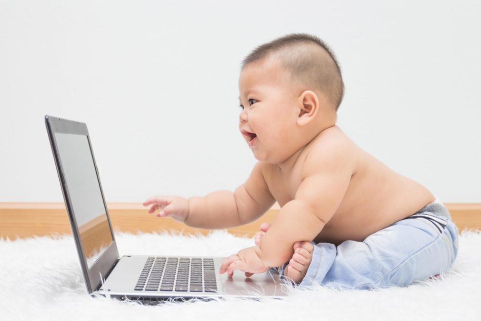Cute baby boy with laptop on white carpet.
