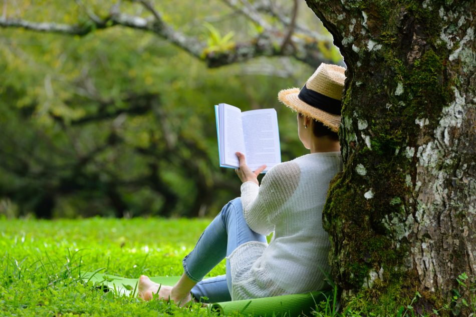 Middle aged woman sitting under a tree reading a book in the park.