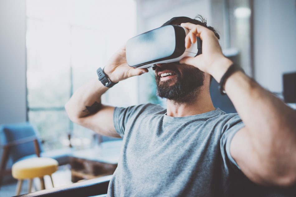 Bearded man wearing virtual reality goggles in modern coworking studio.
