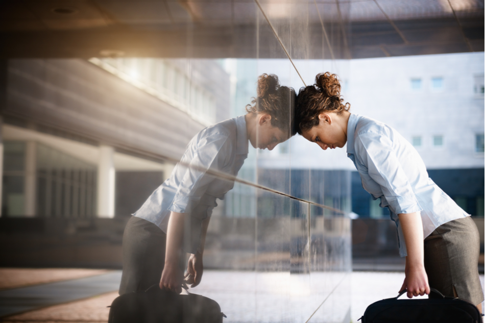 Tired business woman leaning with her head against glass wall of office building