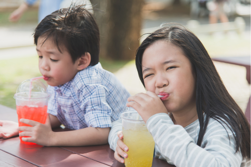 Two cute Asian children sip on sugary drinks