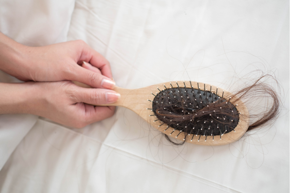 hands hold hairbrush with clump of hair caught in its teeth