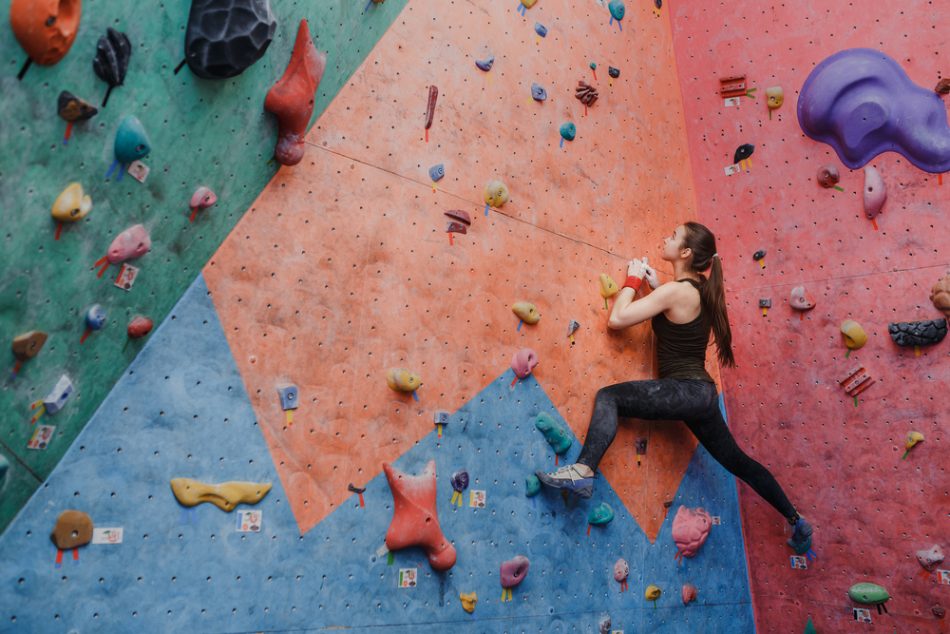 Young fitness woman doing professional bouldering in climbing gym indoors.