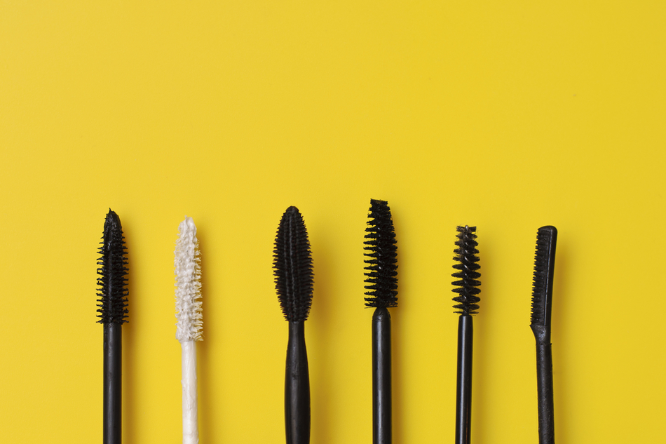 six different mascara wands lay against a bright yellow background