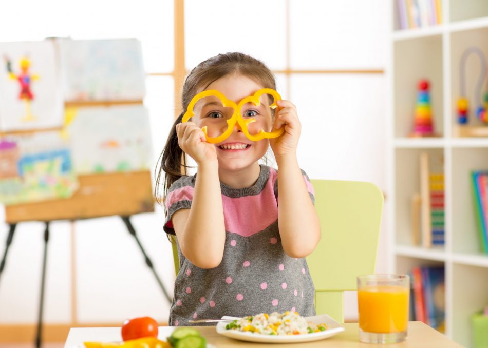little girl holds yellow bell peppers around her eyes
