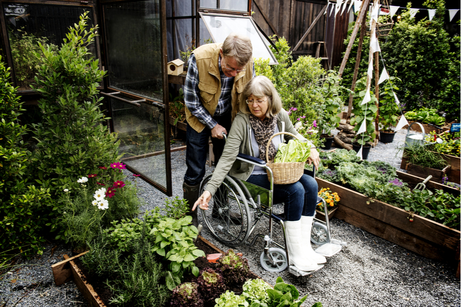 elderly man pushes elderly woman's wheelchair into accessible garden