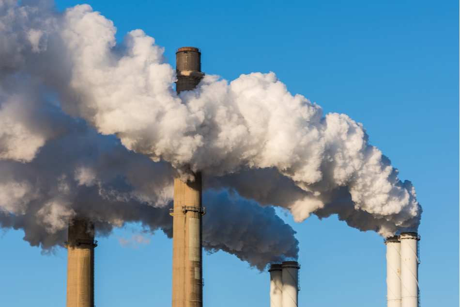 The chimneys of a power station with huge smoke stacks and a blue sky as background.
