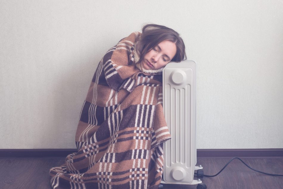 cold girl wrapped in a blanket sits on the floor next to heater