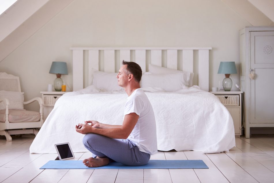 Mature man with digital tablet using meditation app in bedroom.
