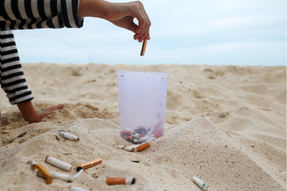 someone picks up littered cigarette butts on the beach