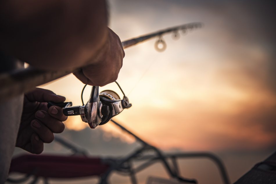 Fishing rod wheel closeup, man fishing with a beautiful sunrise behind him.