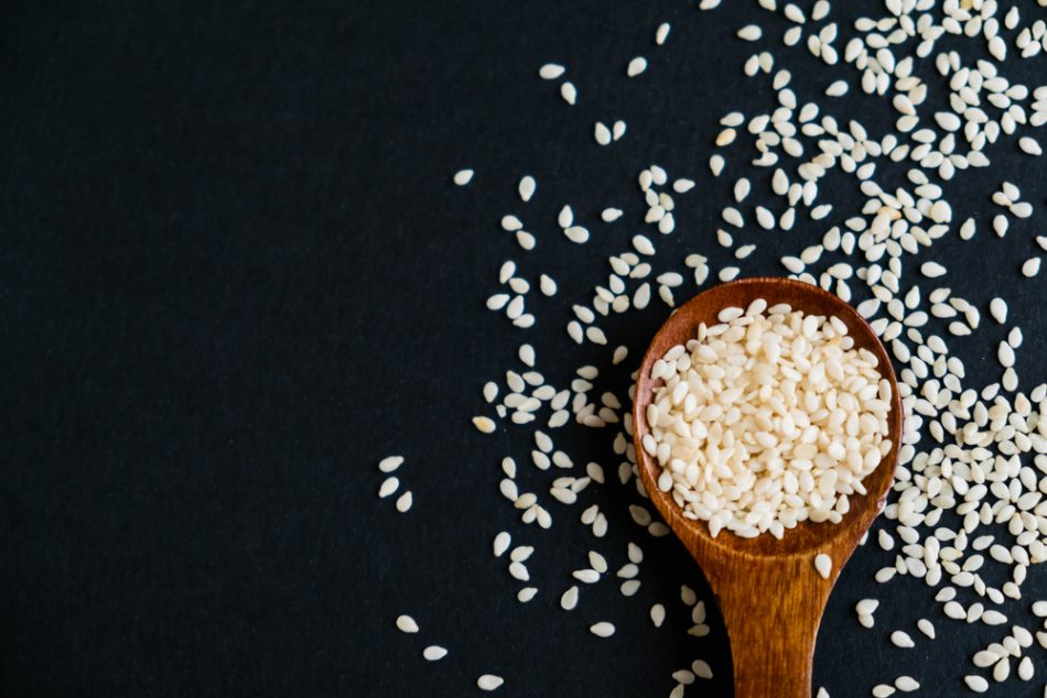 Organic natural sesame seeds on a wooden spoon in front of a black background.