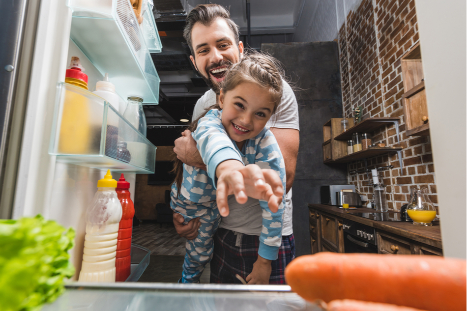 View from inside of fridge of dad and young daughter reaching inside for food