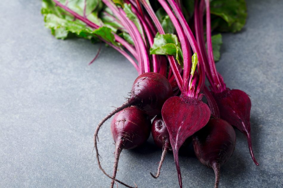 a bushel of beets with vibrant leafy green stems lays on a grey countertop