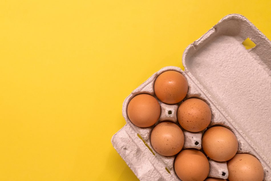 Overhead view of brown chicken eggs in an open egg carton isolated on a yellow background.