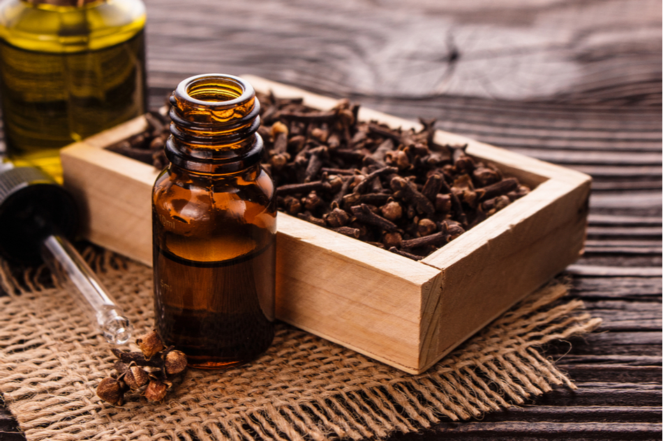 Clove essential oil on a wooden table next to a container with cloves