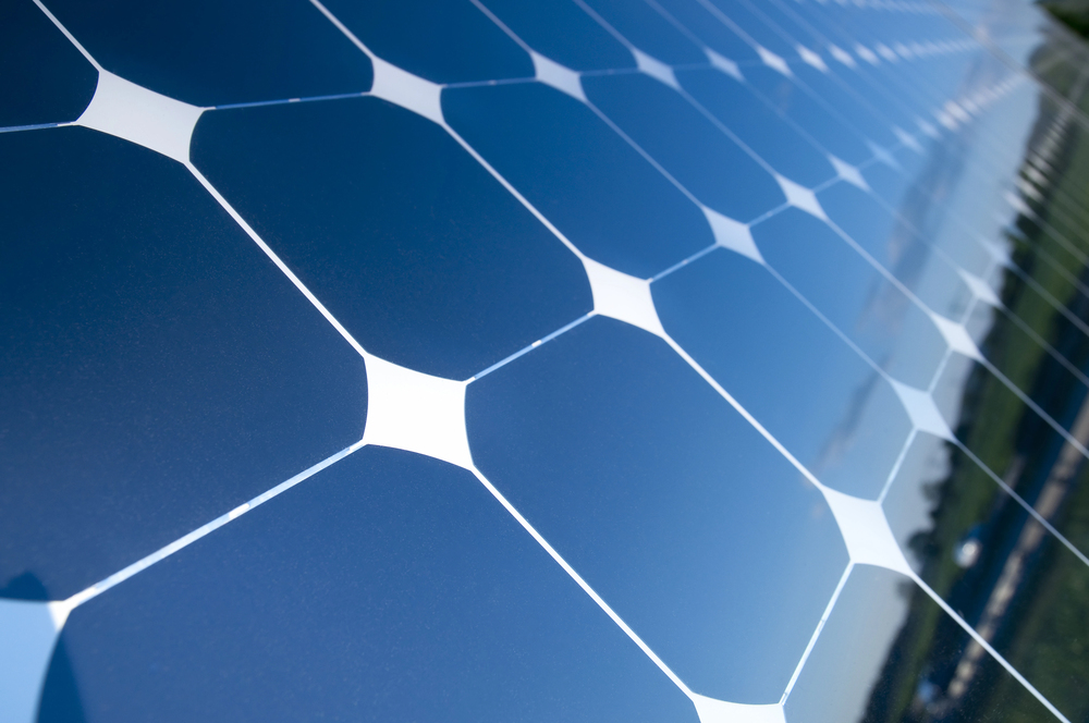 Close-up of a blue solar panel array with reflective hexagonal cells against a clear sky surface edge visible on the right side