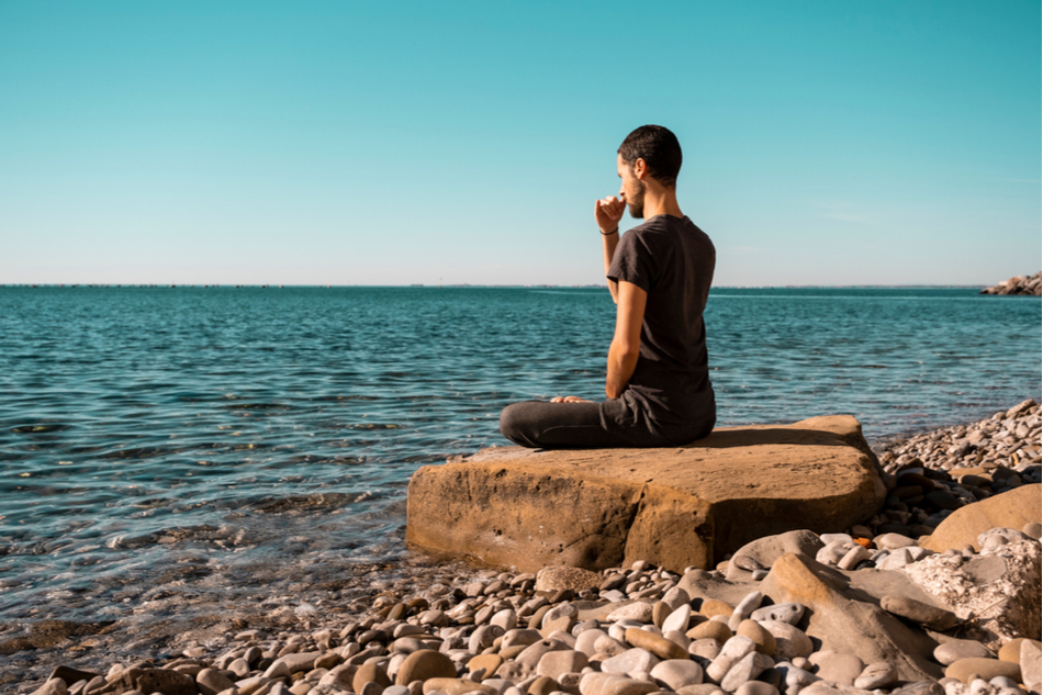 Young man sitting on a rock on a beach doing breath exercises